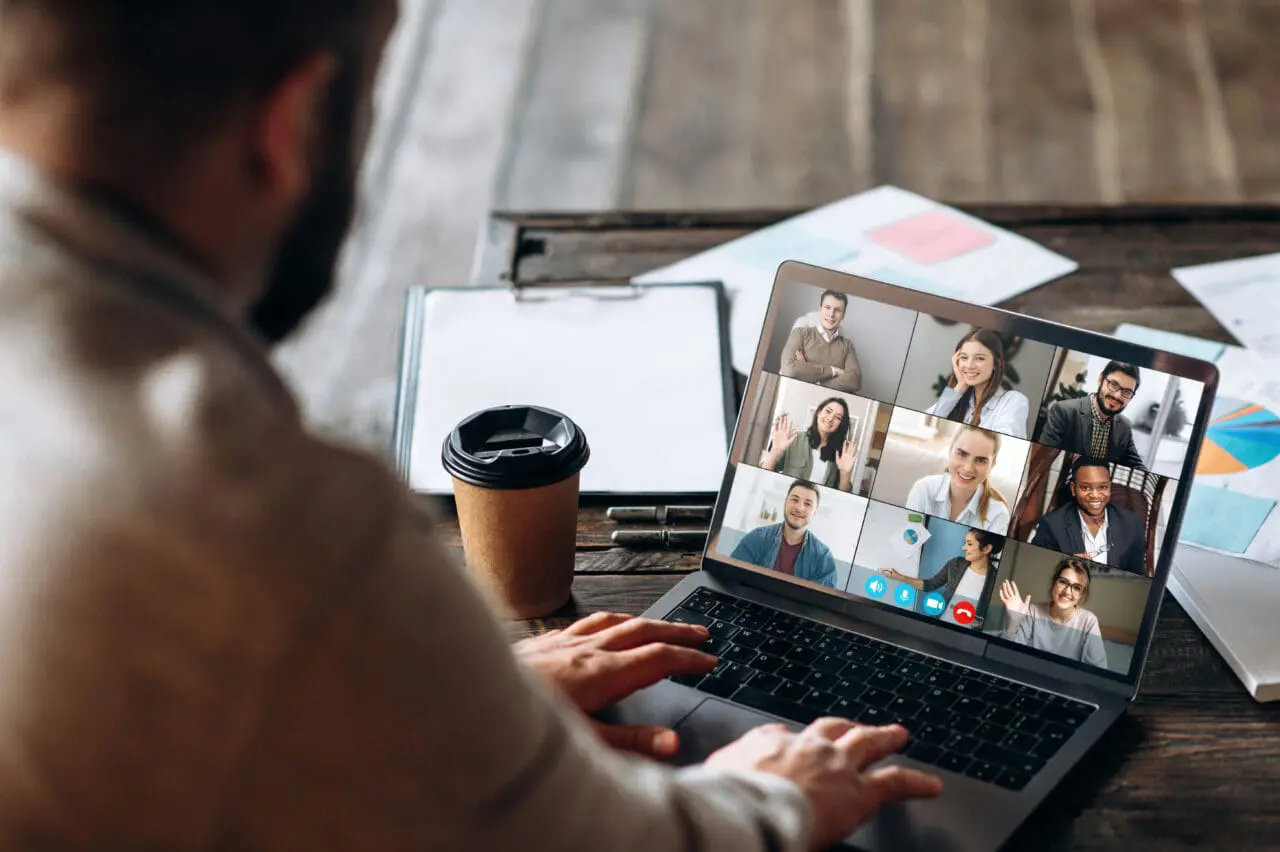 Close up of man sat at home desk, on conference call with colleagues, on Mac laptop