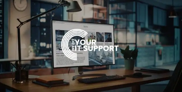 WeDoYourITSupport white logo on background of a computer screen monitor on wooden desk, in dimly lit room