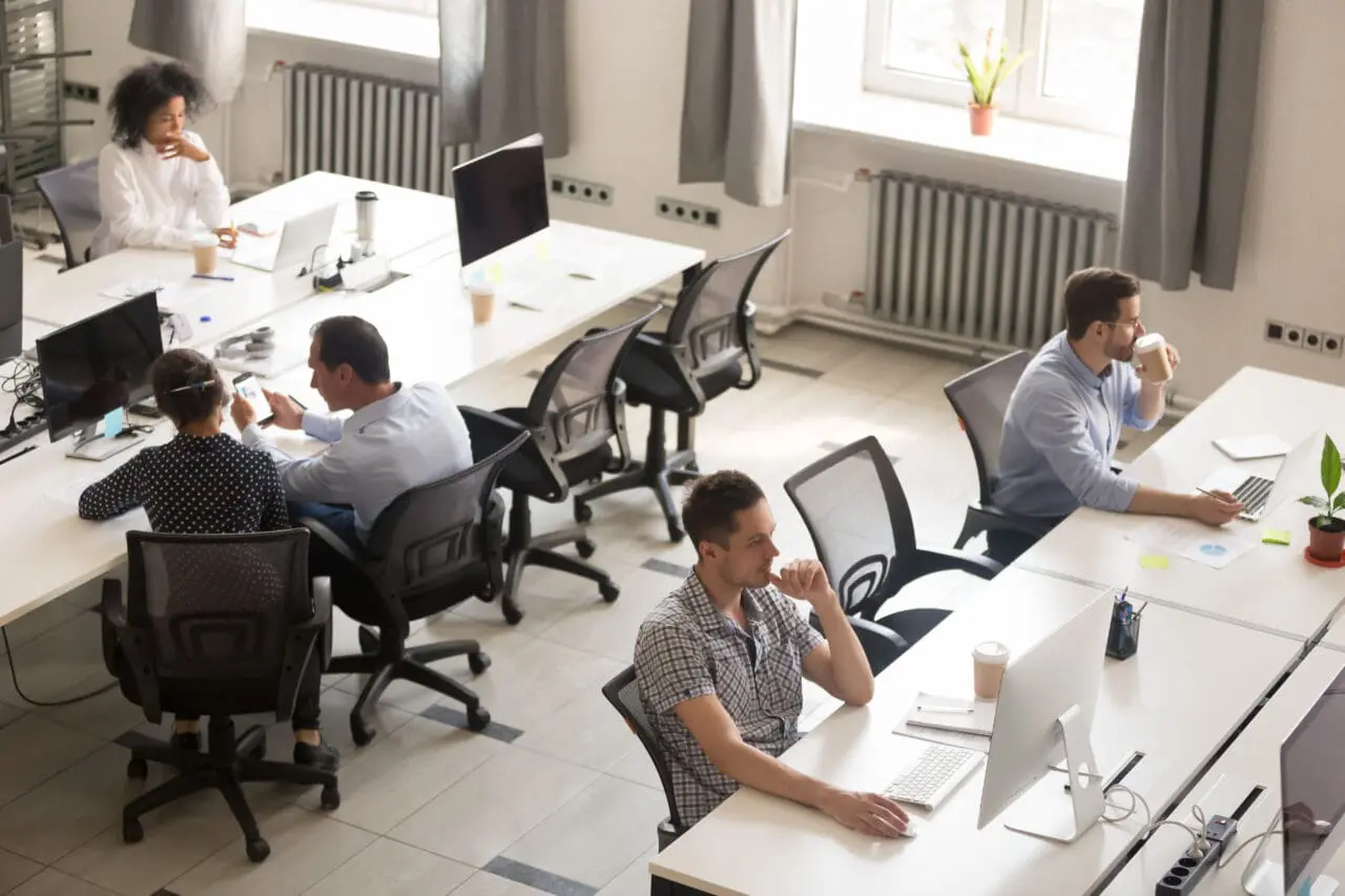 Modern office with workers on Mac laptops and computers. Coffee cups and plants on desks