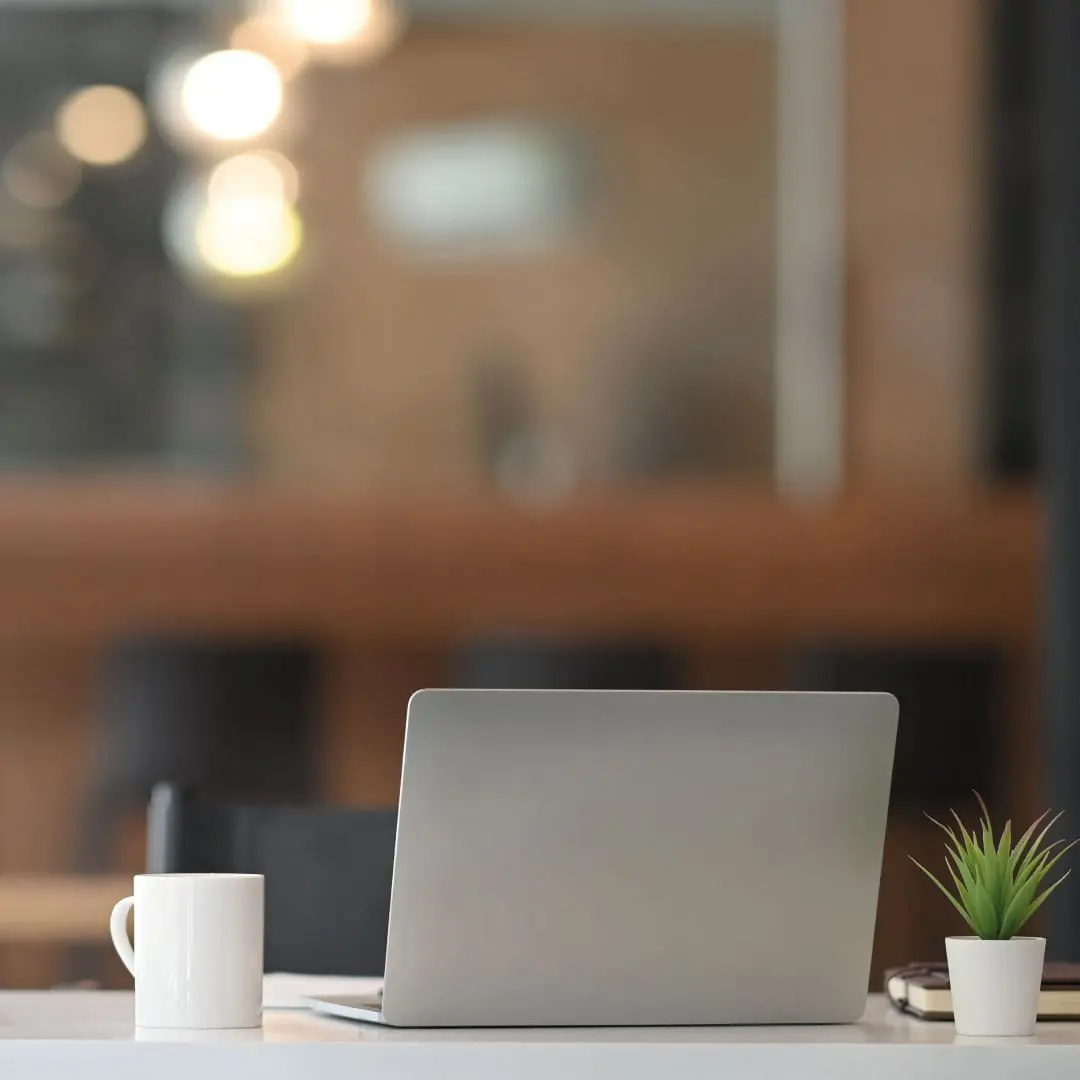 Mac laptop on desk with coffee cup and plant beside it