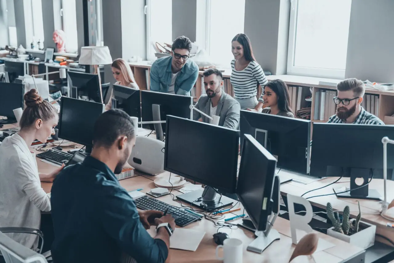 Group of workers, talking, smiling and working together at their desks