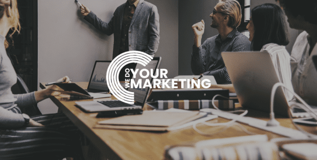 WeDoYourMarketing white logo on background of group of workers in office, discussing graphs