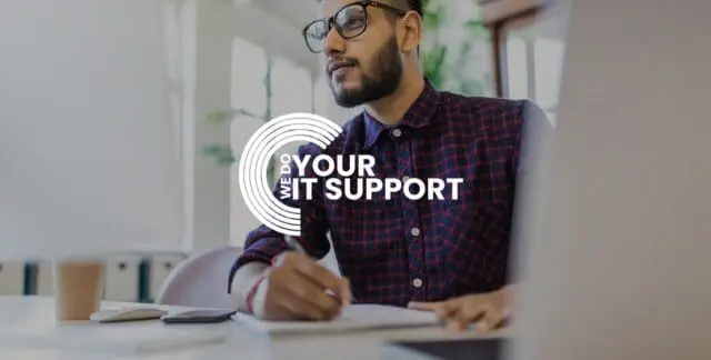 WeDoYourITSupport white logo on background of man writing on notebook, with Mac laptop in front of him