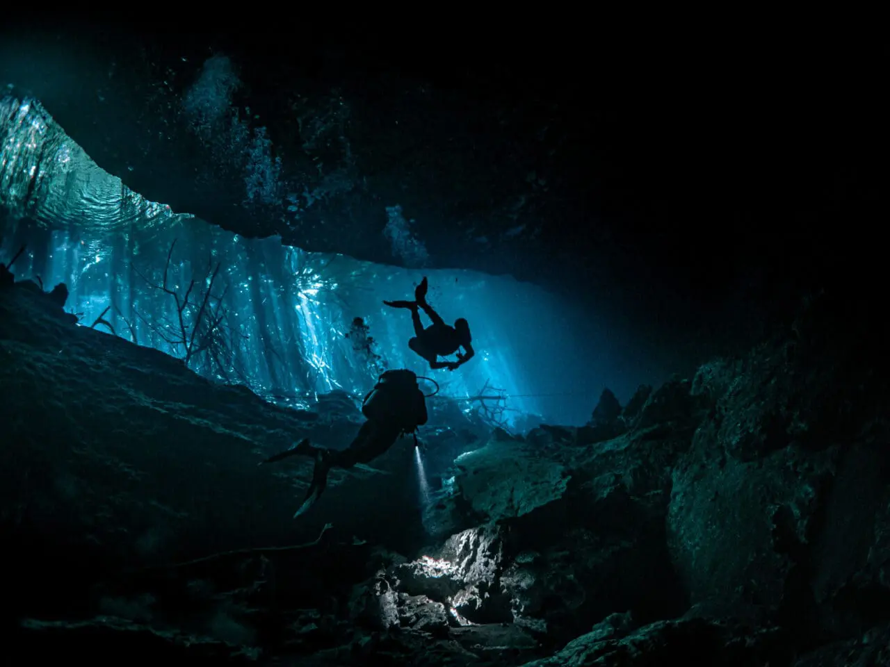 Deep sea scuba divers surrounded by rocks underwater