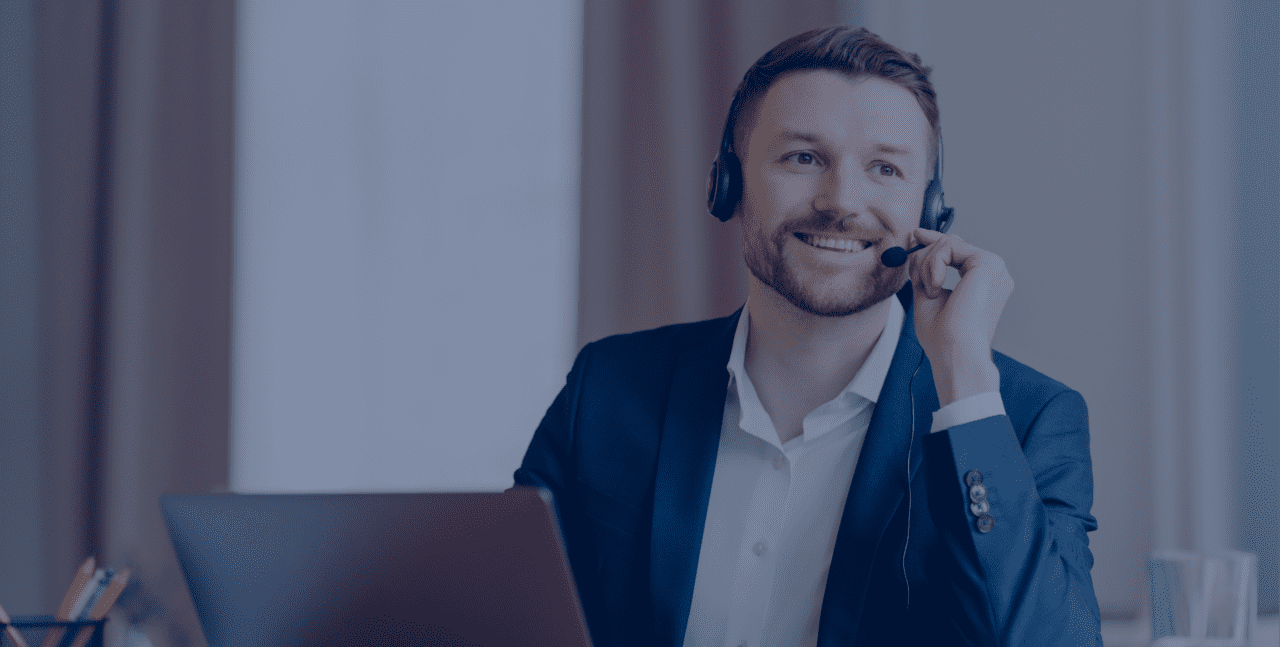 Photo of happy male manager wears headset works on laptop computer consults clients looks with glad thoughtful expression away dressed formally poses at desktop. Support and online consultation