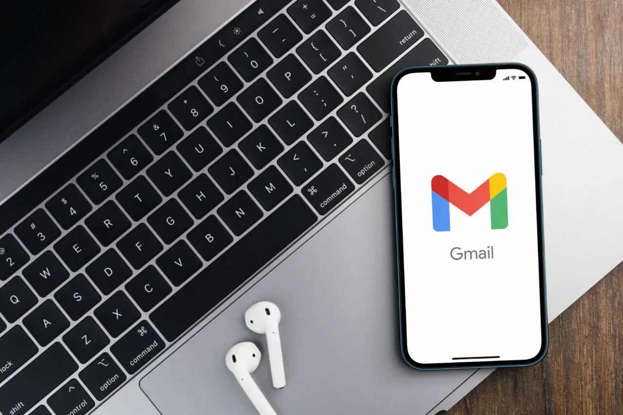Gmail app on the smartphone screen on wooden background with a computer beside it. Top view.