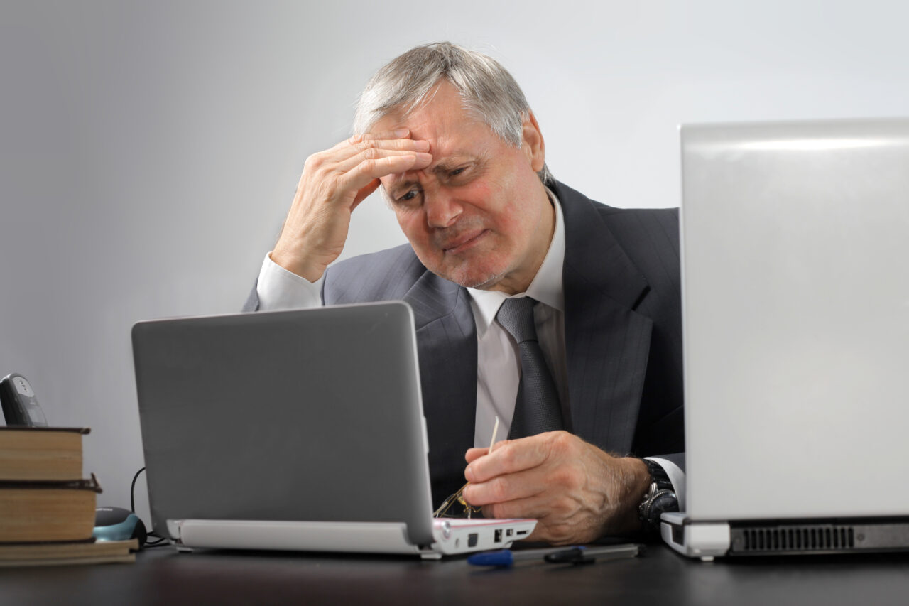 Older man in suit sat at desk, looking at his laptop