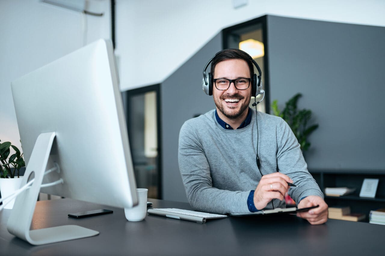 Agent taking notes while talking with customer using headphones and microphone in customer support center.