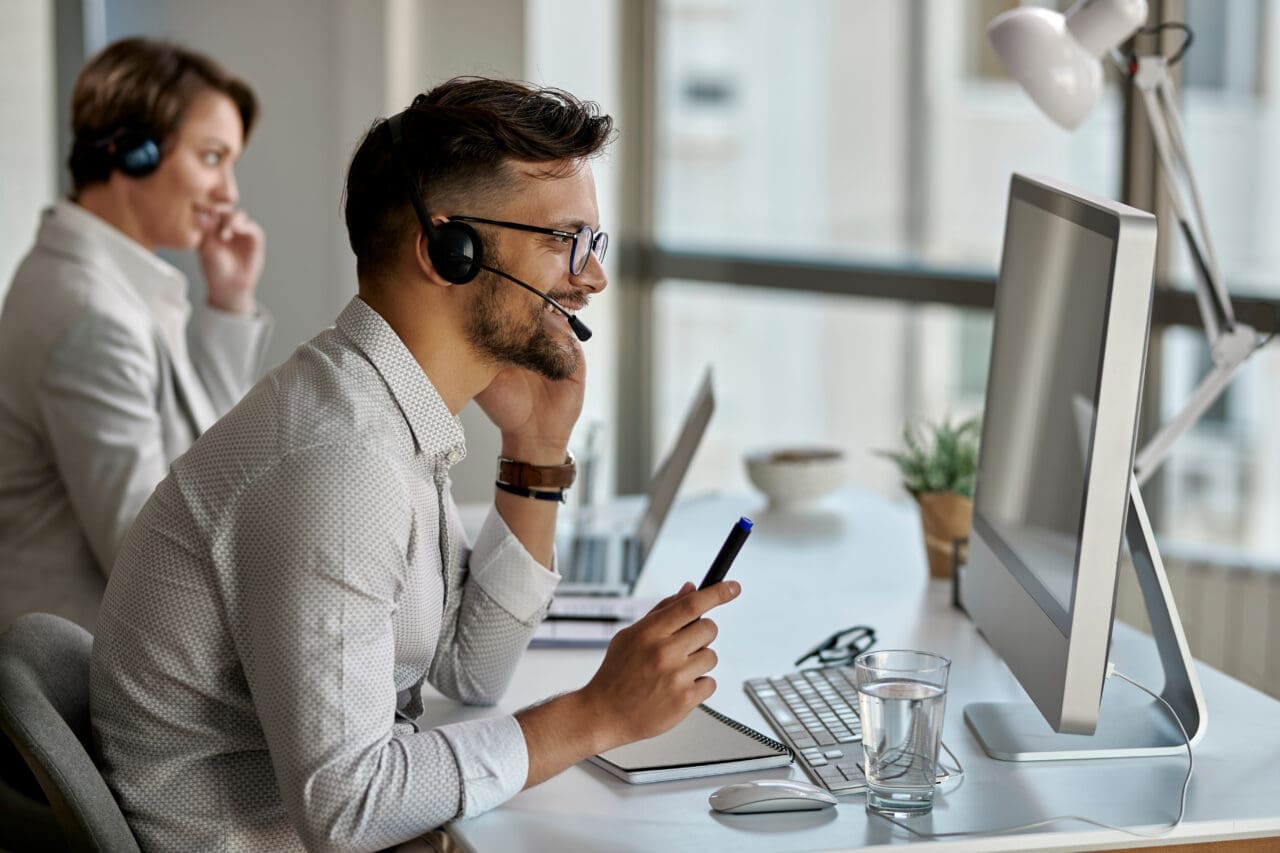 Happy call center agent using computer while communicating with clients in the office.