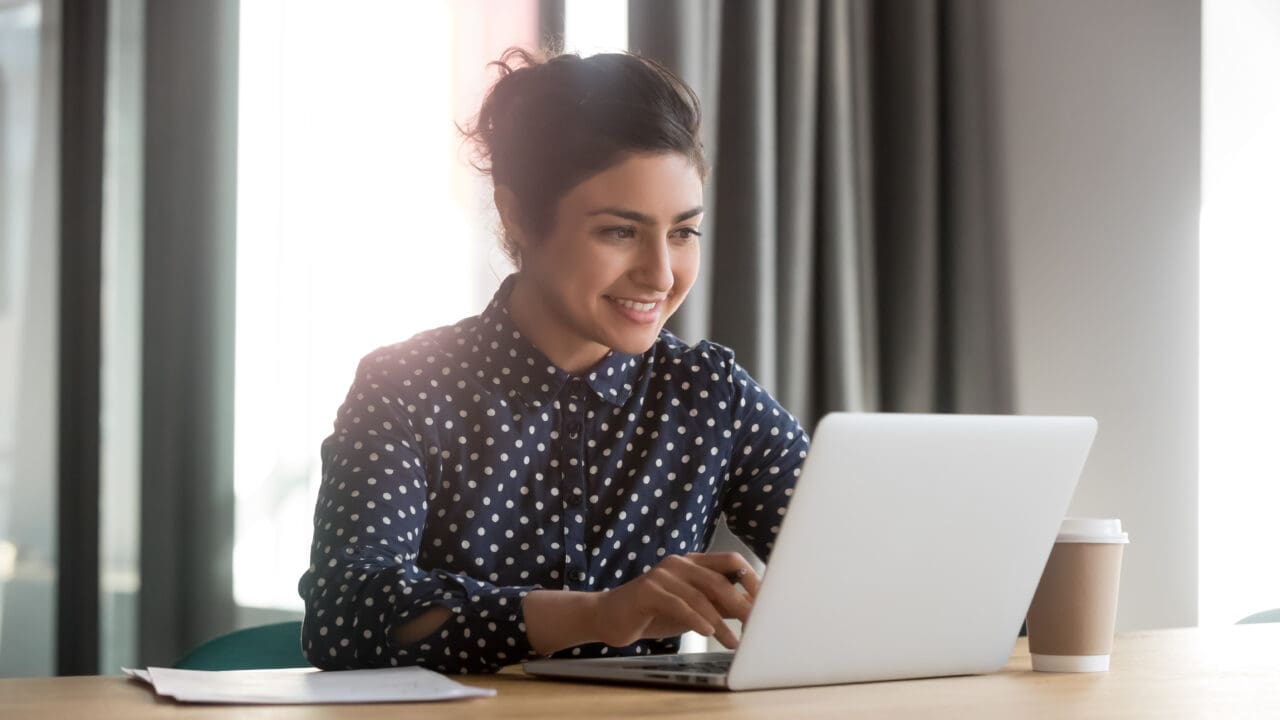 Happy young businesswoman using computer sitting at office desk