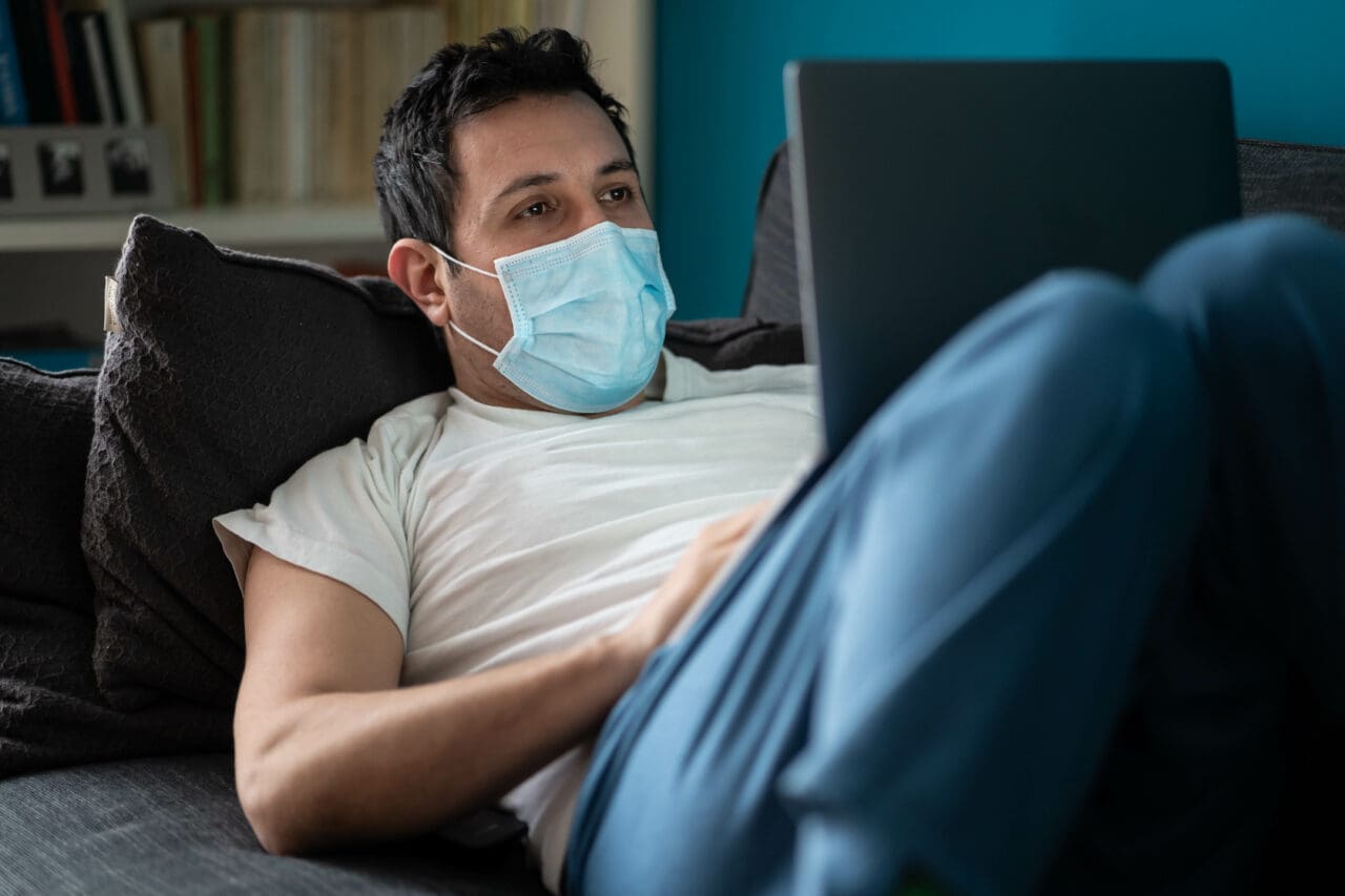 Man is working from home on his sofa, using laptop, during Coronavirus or Covid-19
