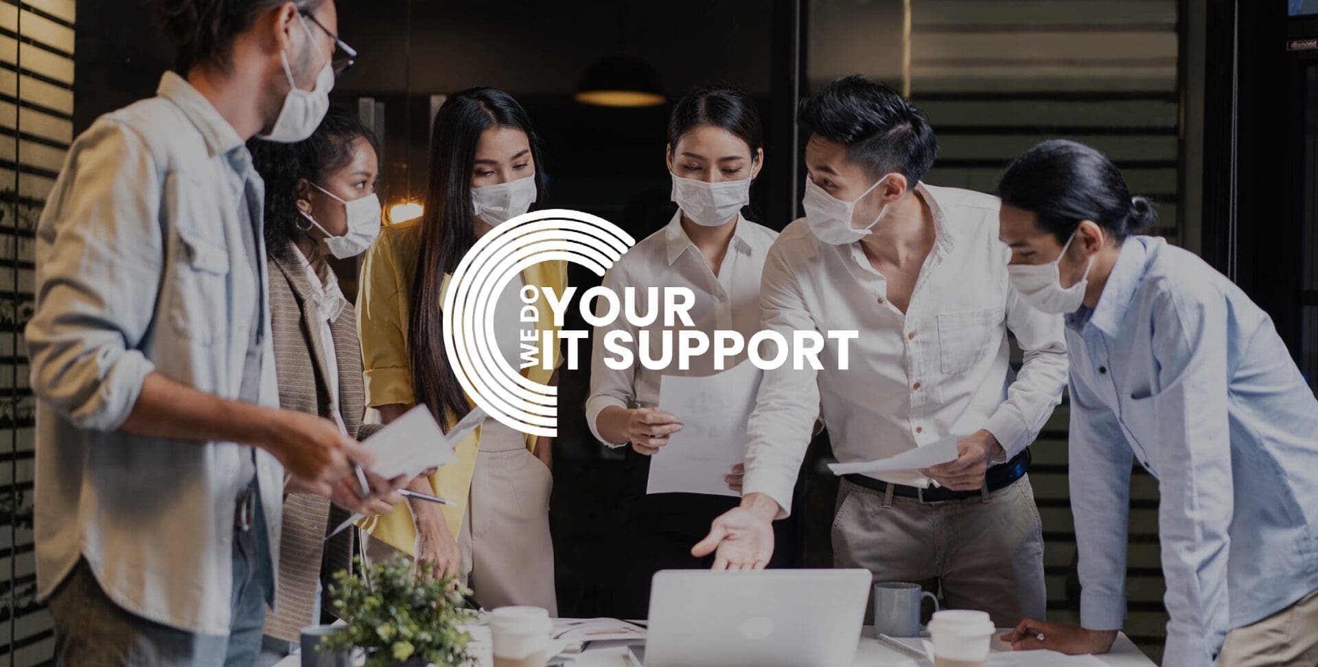 WeDoYourITSupport white logo on background of group of workers stood around a desk, all wearing face masks