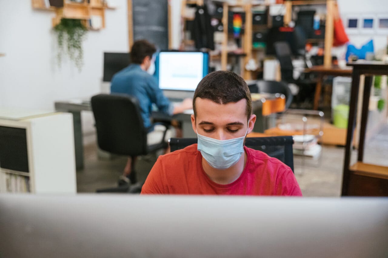Man with surgical mask working at computer in office, wearing a face mask