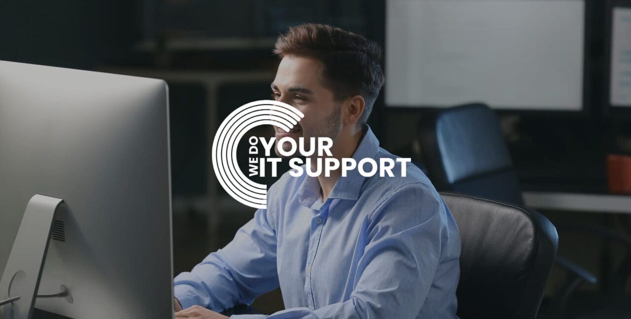 WeDoYourITSupport white logo on background of smiling business man sat working on Mac computer