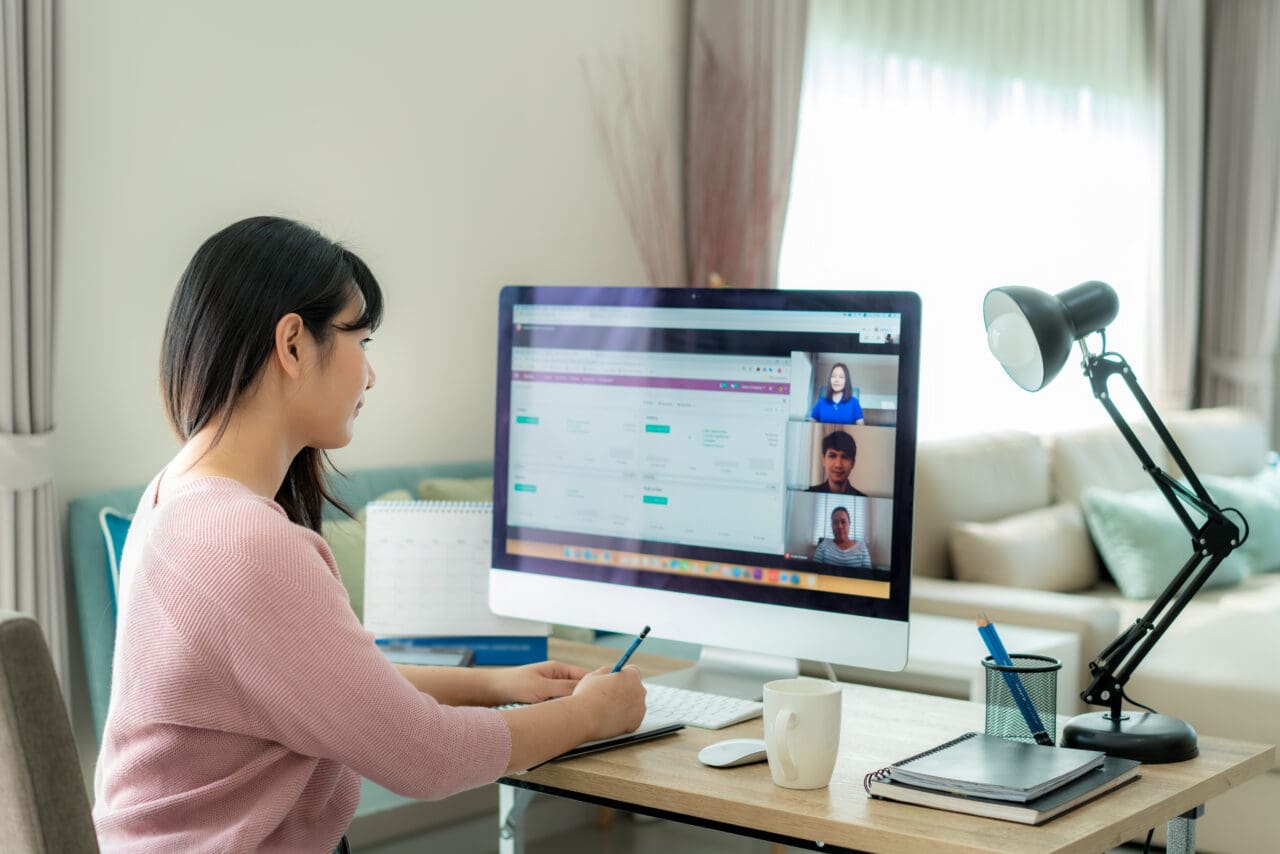 Back view of Asian business woman talking to her colleagues on a video call. Using a Mac computer on her desk