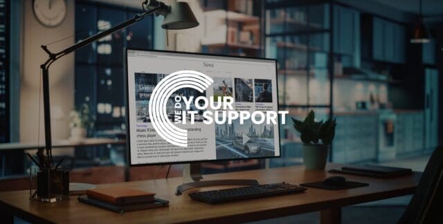 WeDoYourITSupport white logo on background of a computer screen monitor on wooden desk, in dimly lit room