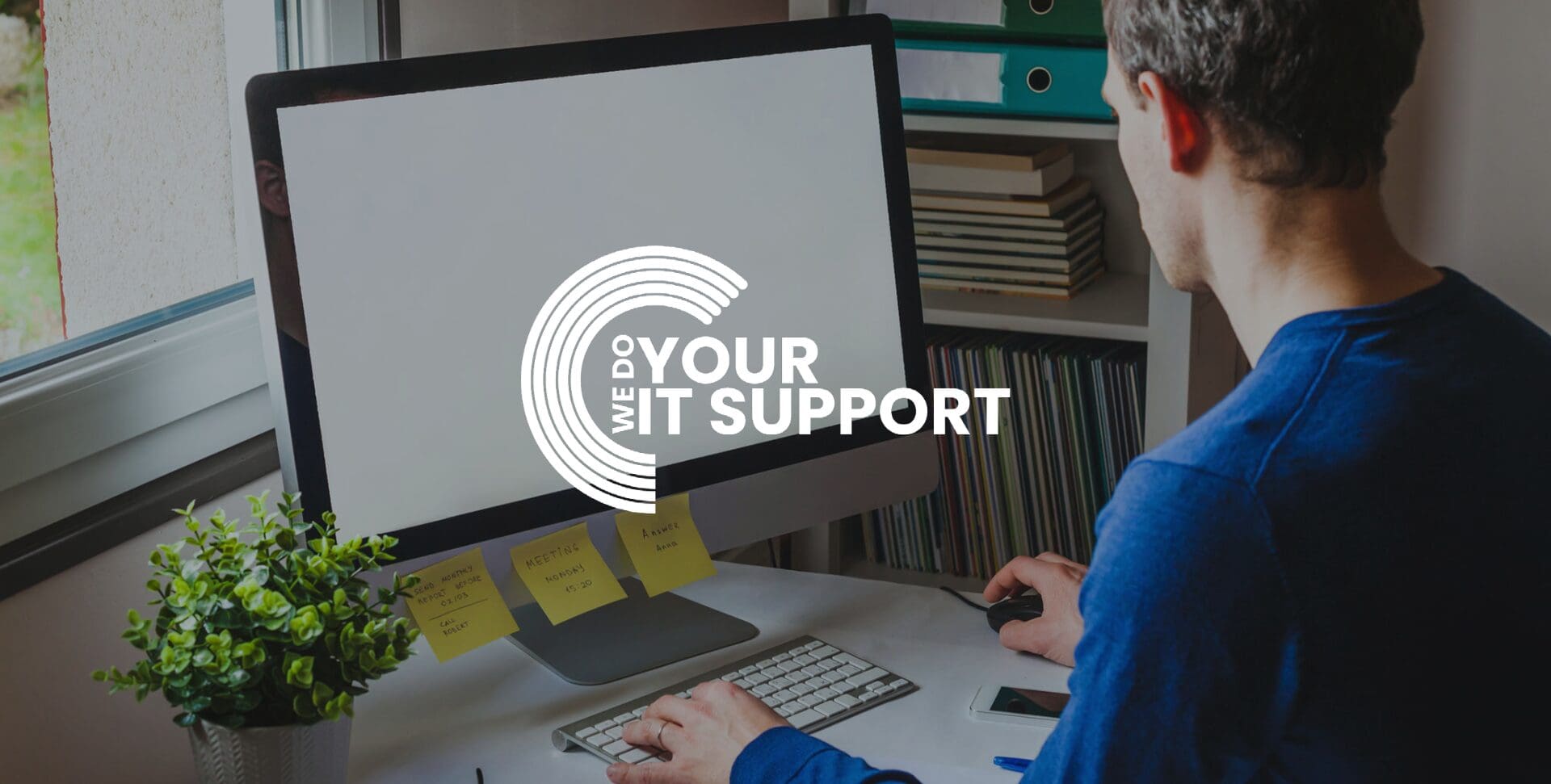 WeDoYourITSupport white logo on background of man sat at home desk, with Mac computer