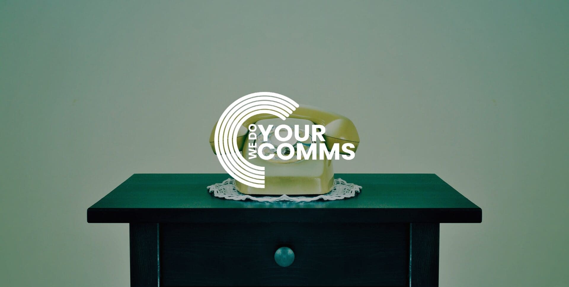 WeDoYourComms white logo on background of green olds style telephone placed on green side table