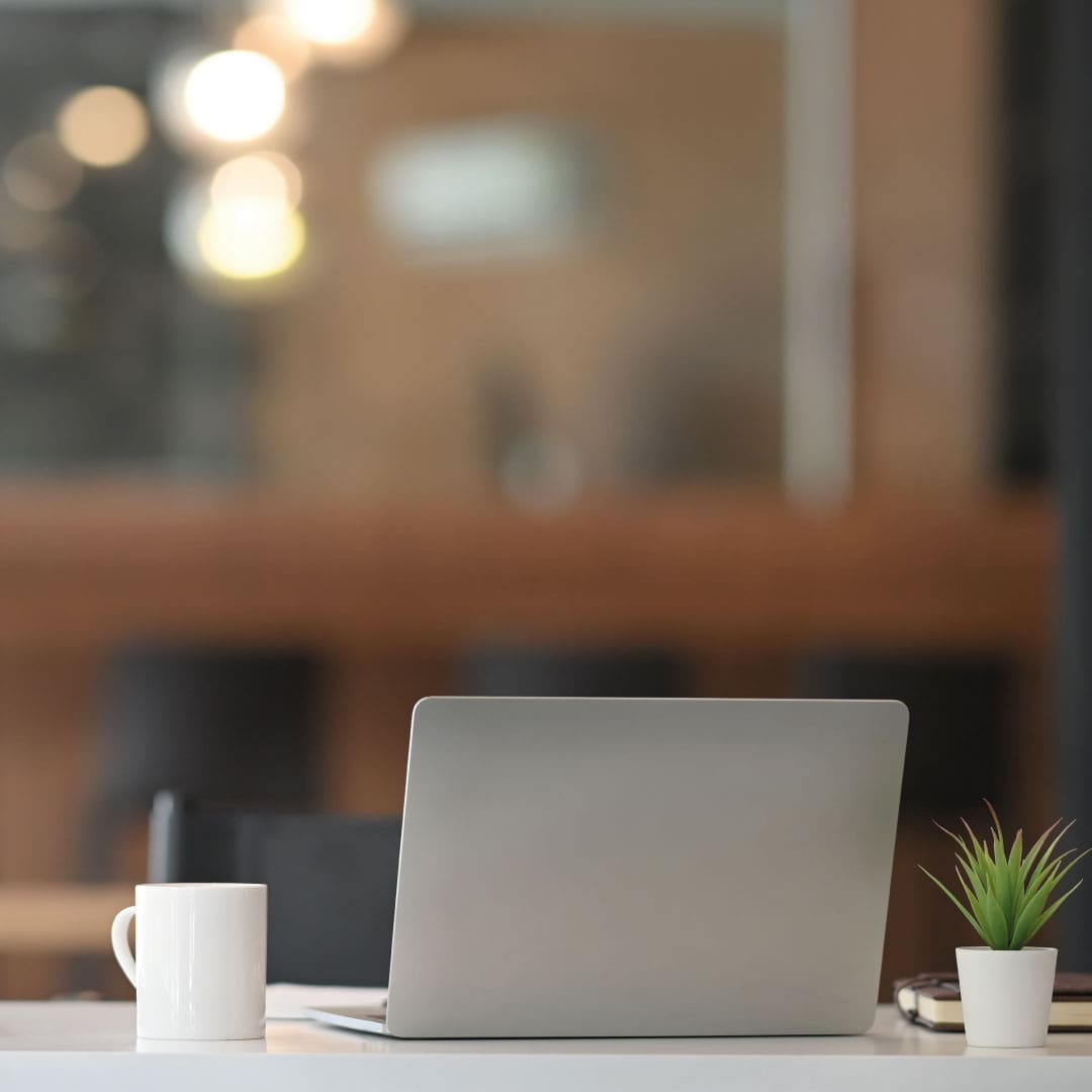 Mac laptop on desk with coffee cup and plant beside it