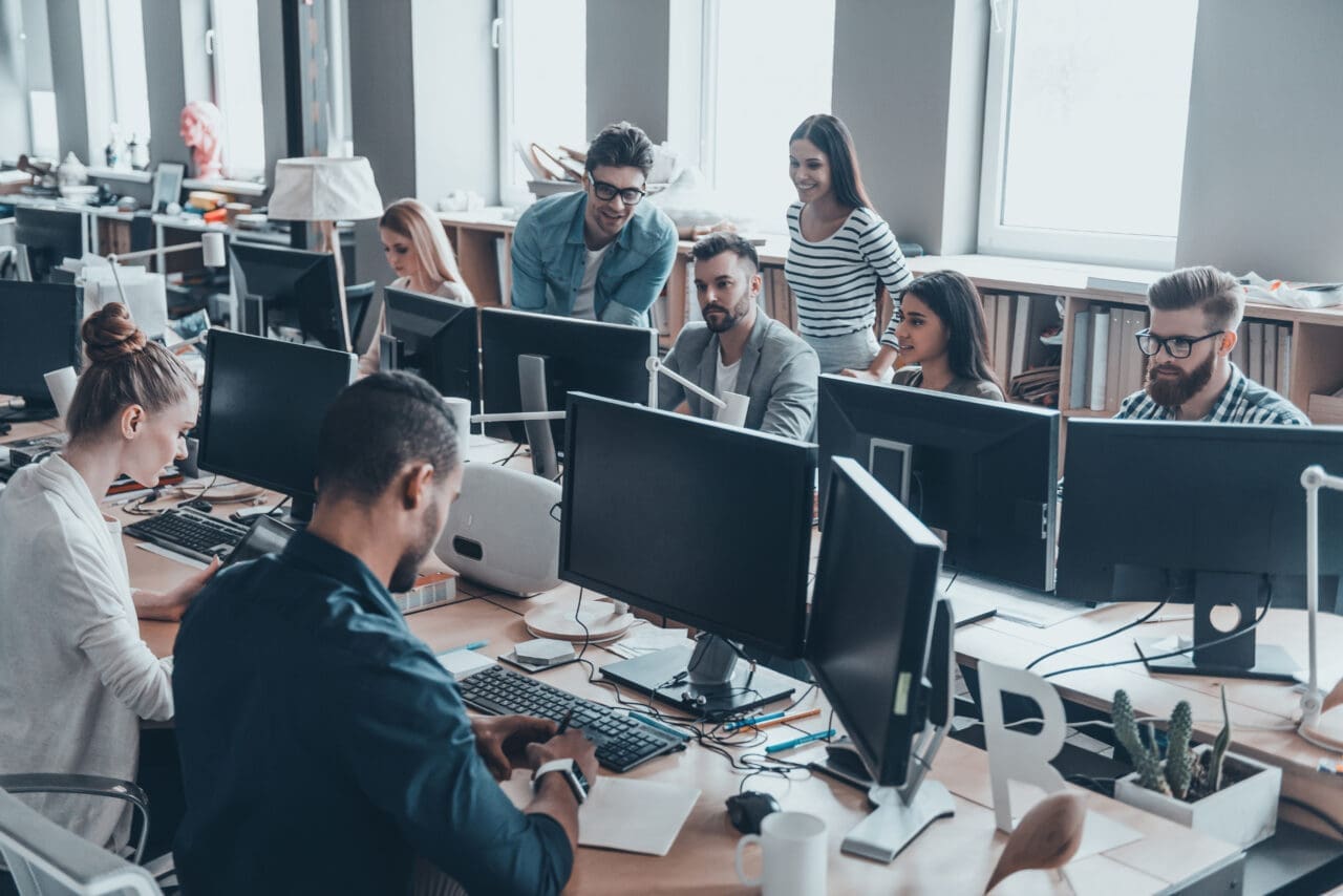 Group of workers, talking, smiling and working together at their desks