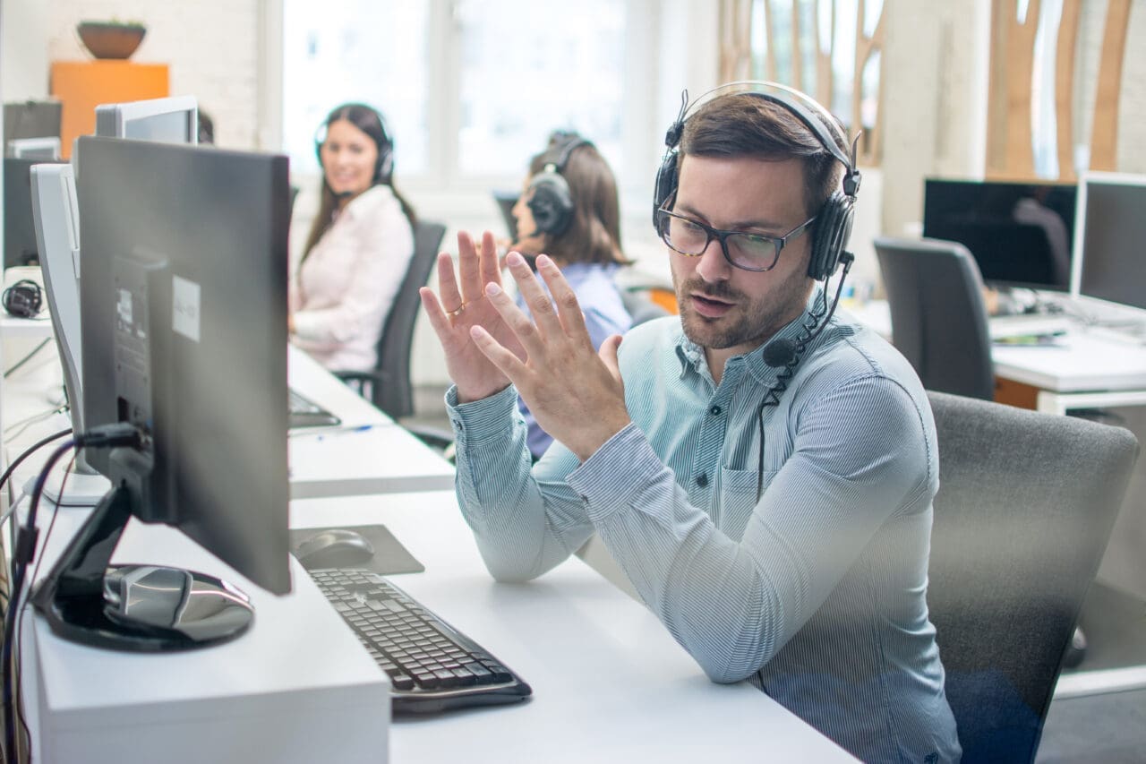 Young male technical support agent trying to explain something to a customer on a telephone headset