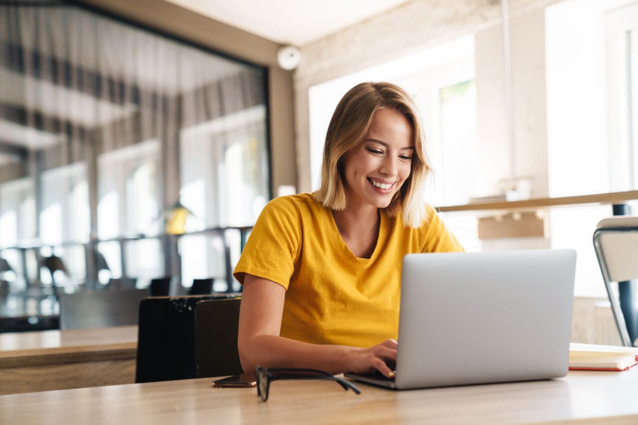 Photo of joyful nice woman using Mac laptop and smiling while sitting in office