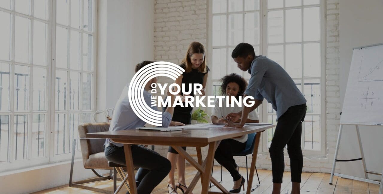 WeDoYourMarketing white logo on background on colleagues talking and working together at a desk