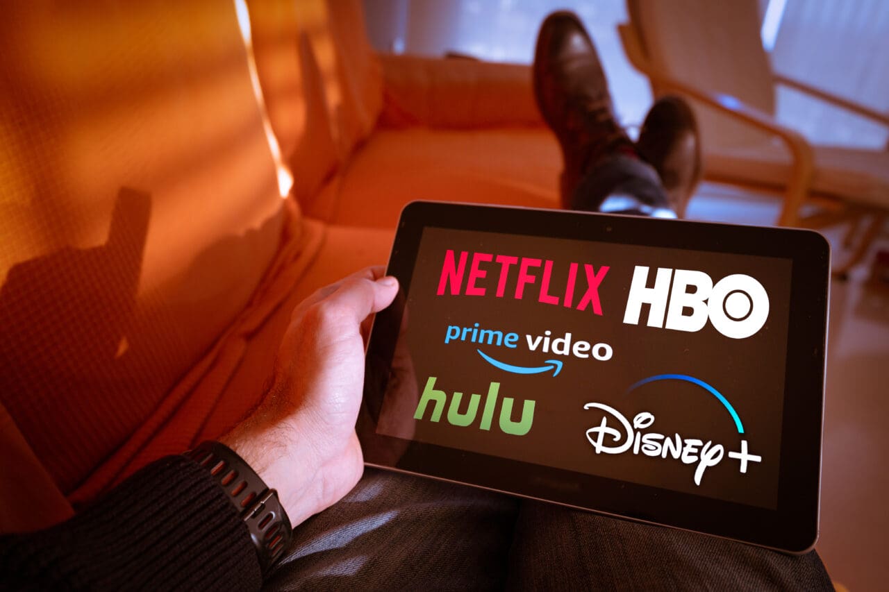 Man holds a tablet with Netflix, hulu, amazon video, HBO and Disney+ logos on screen