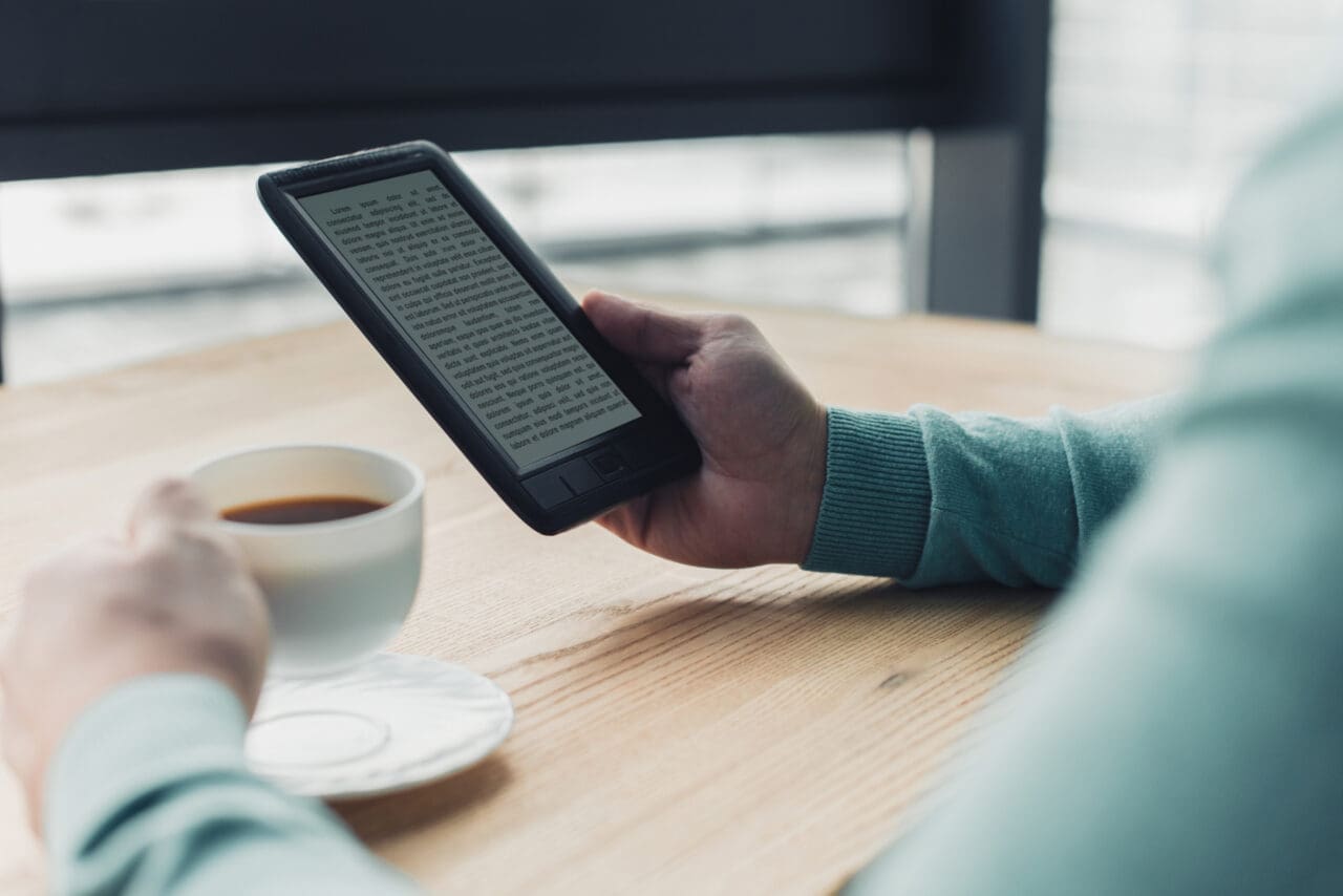 cropped view of man holding cup of tea near e-reader while studying