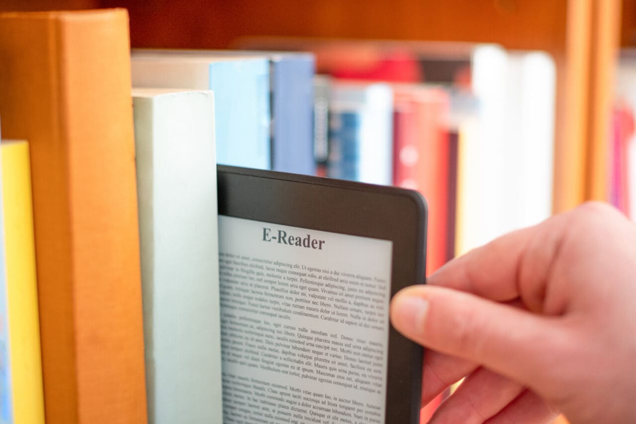 Hand of student keeping digital tablet in bookshelf in school library
