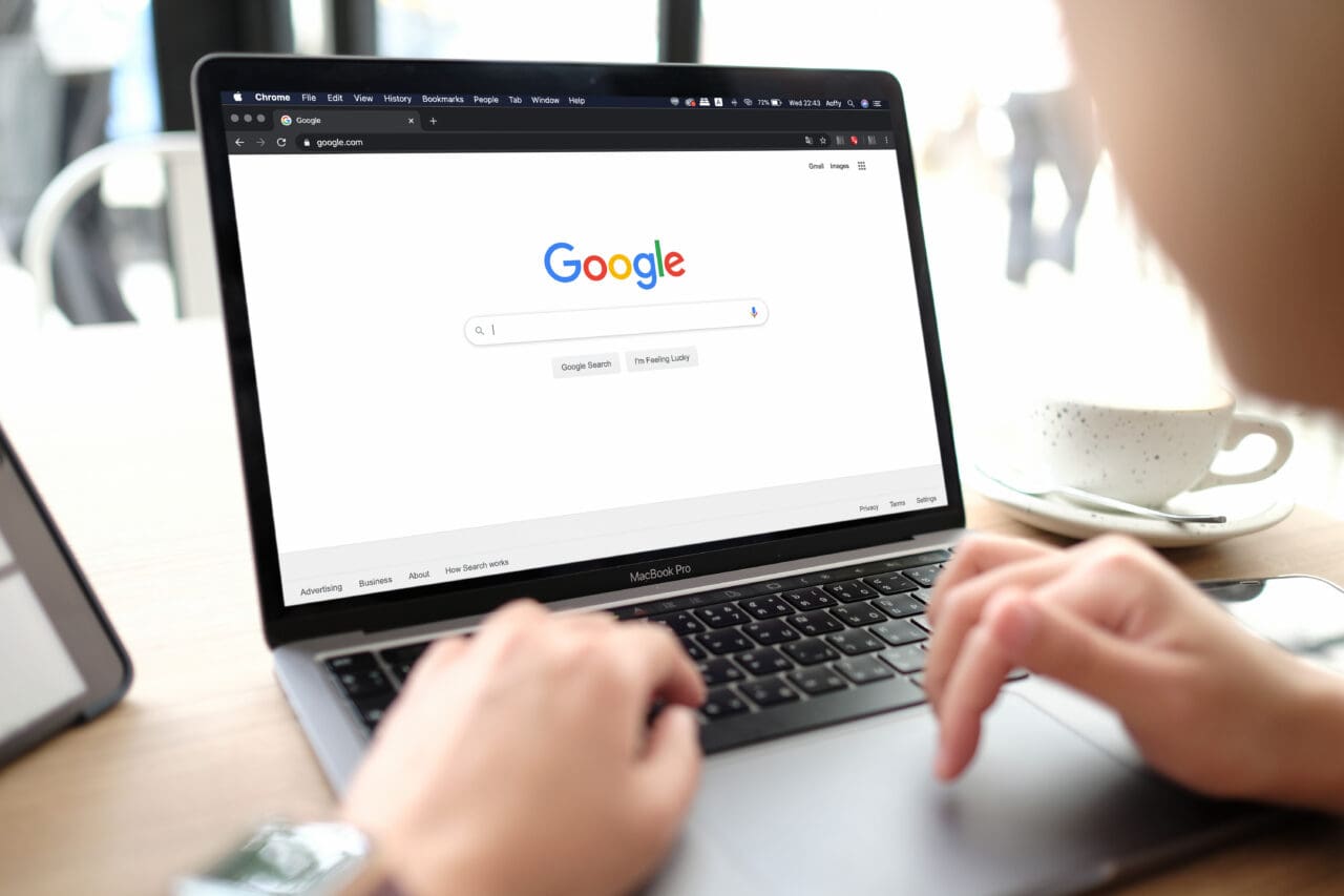 A man typing on Google search on a Mac laptop