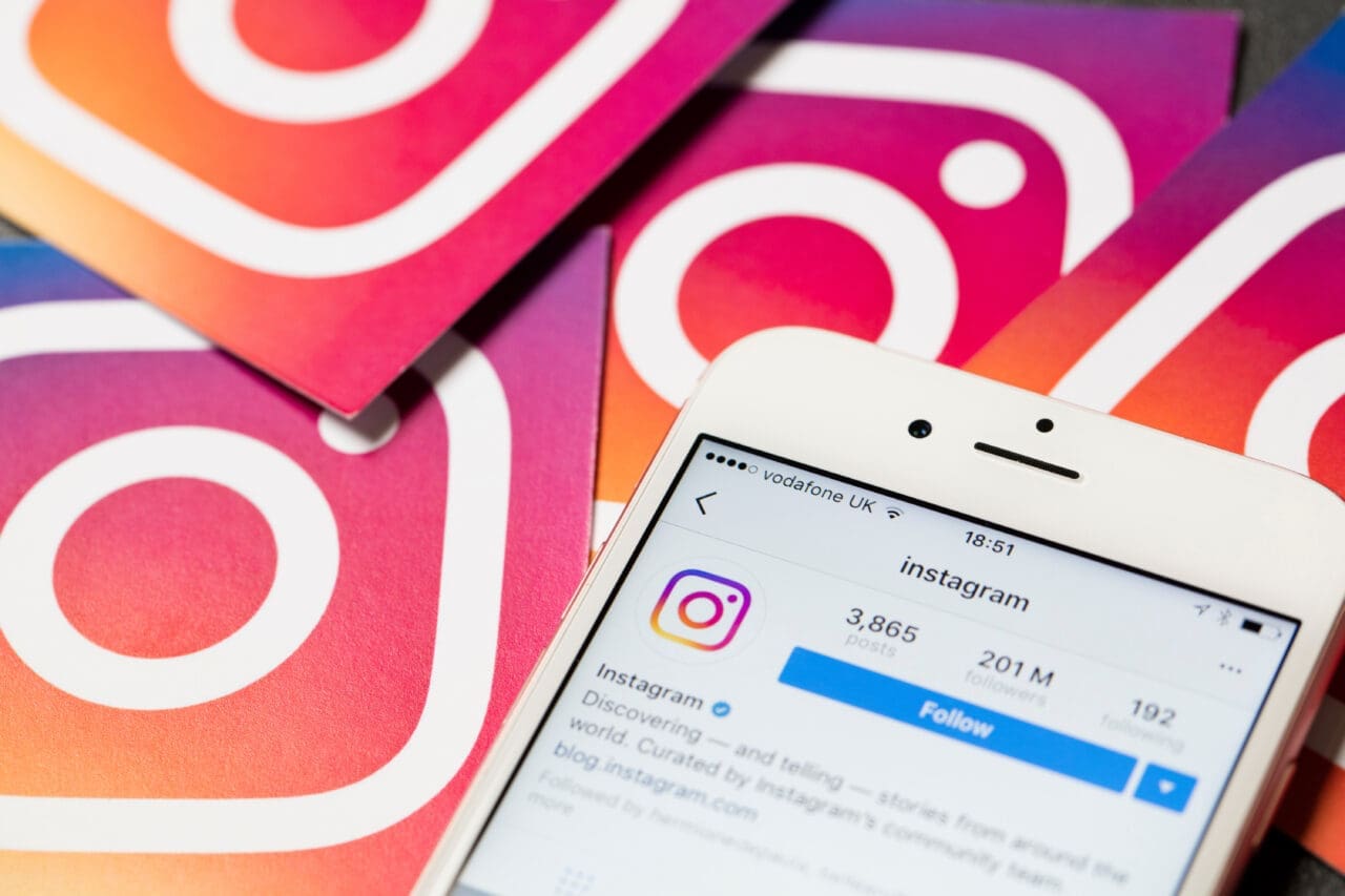 iPhone with Instagram app open on the screen with Instagram logos in the background