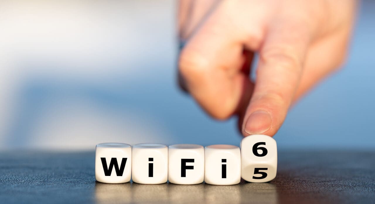 Hand turns dice and changes the expression "WiFi 5" to "WiFi 6".