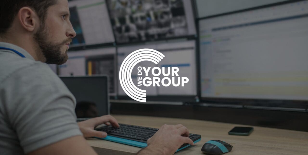 WeDoYourGroup white logo on background of man sat at desk working on multiple monitors