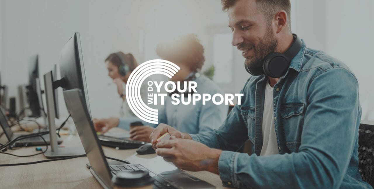 WeDoYourITSupport white logo on background of man smiling sat at his desk working