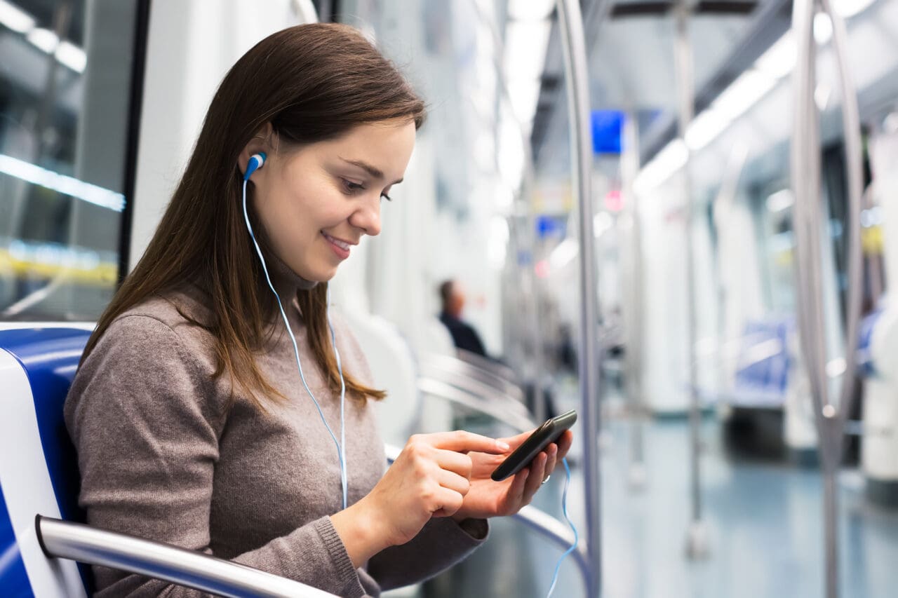 Woman with smartphone at subway, headphones on smiling