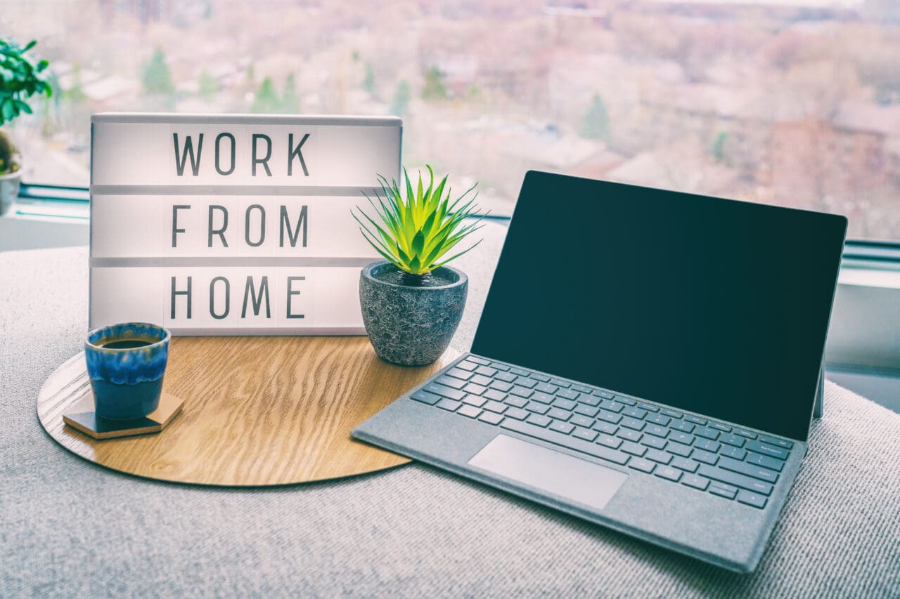Laptop placed on sofa, with a 'work from home' light up sign next to it, with plant