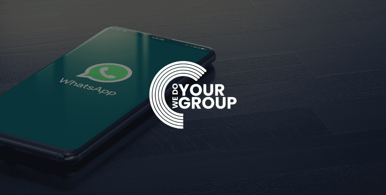 WeDoYourGroup white logo on background of a mobile phone placed on desk with WhatsApp open on the screen