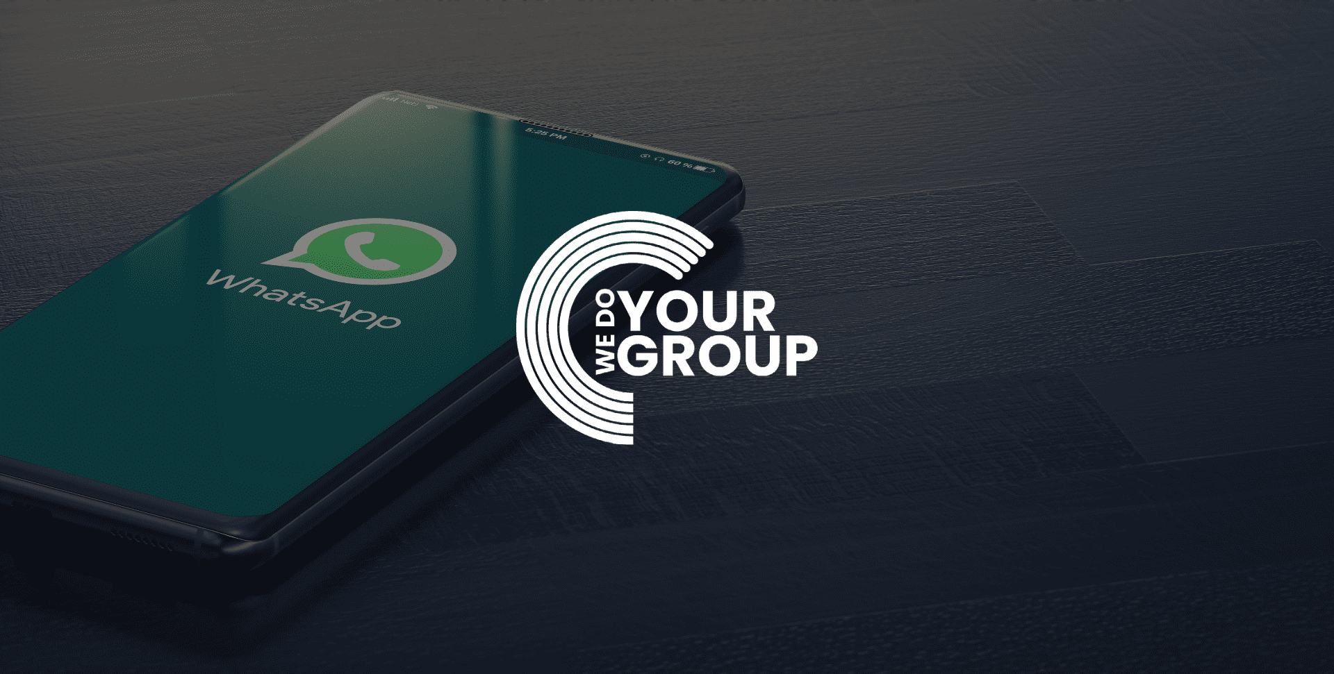 WeDoYourGroup white logo on background of a mobile phone placed on desk with WhatsApp open on the screen