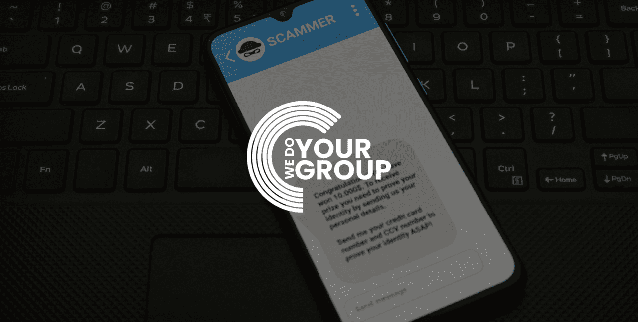 WeDoYourGroup white logo on background of mobile phone with scammer message placed on laptop keyboard.