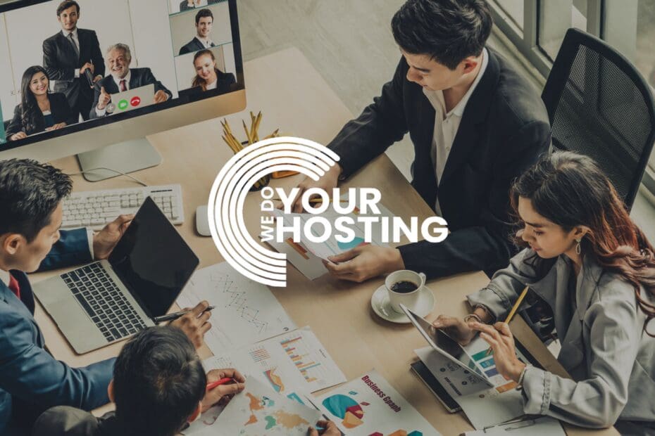 WeDoYourHosting white logo on background with workers sat at a desk together with paper graphs on desk. Mac monitor showing a video call with other workers on screen