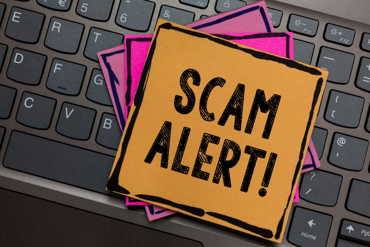 SCAM ALERT written on yellow notice post it note, placed on laptop