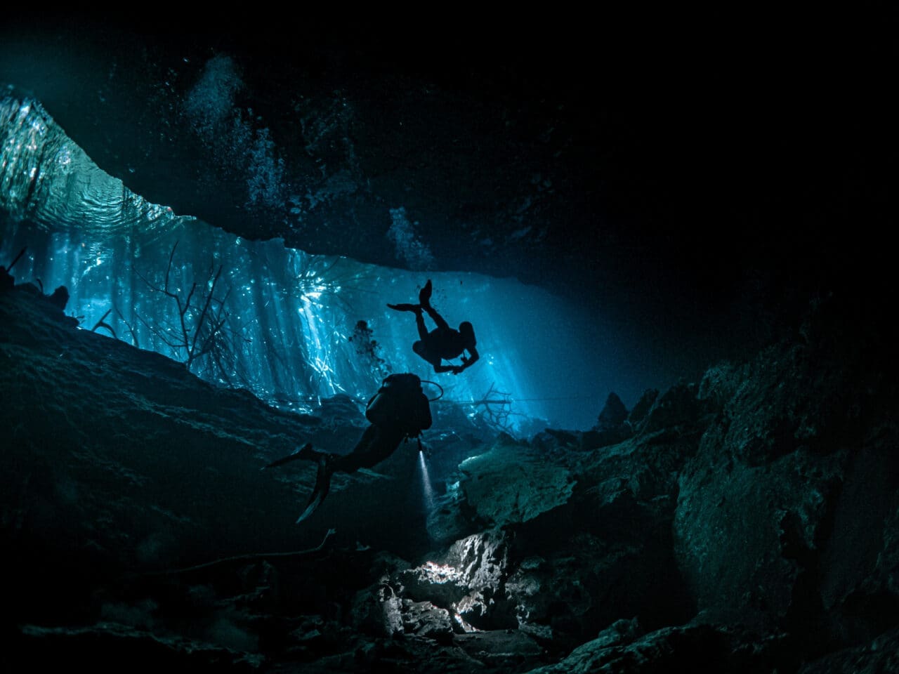 Deep sea scuba divers surrounded by rocks underwater