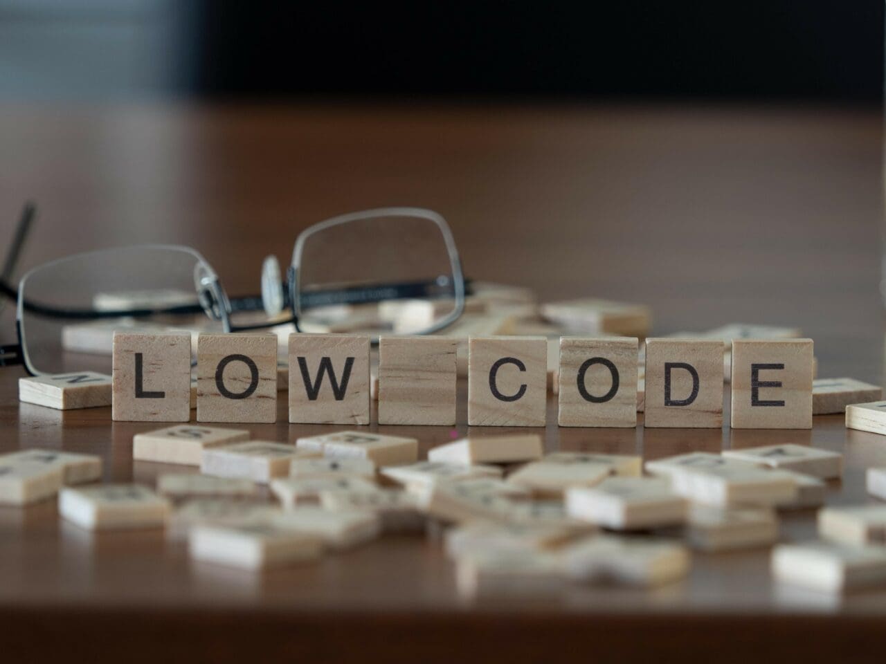 Small wooden blocks with 'Low Code' written on them, placed on a desk with glasses in the background
