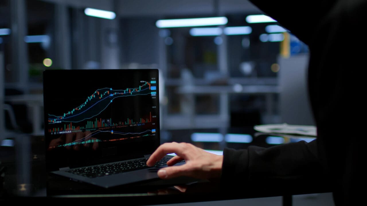 Young sly man trying to breach the system while giving commands on laptop in empty dark office