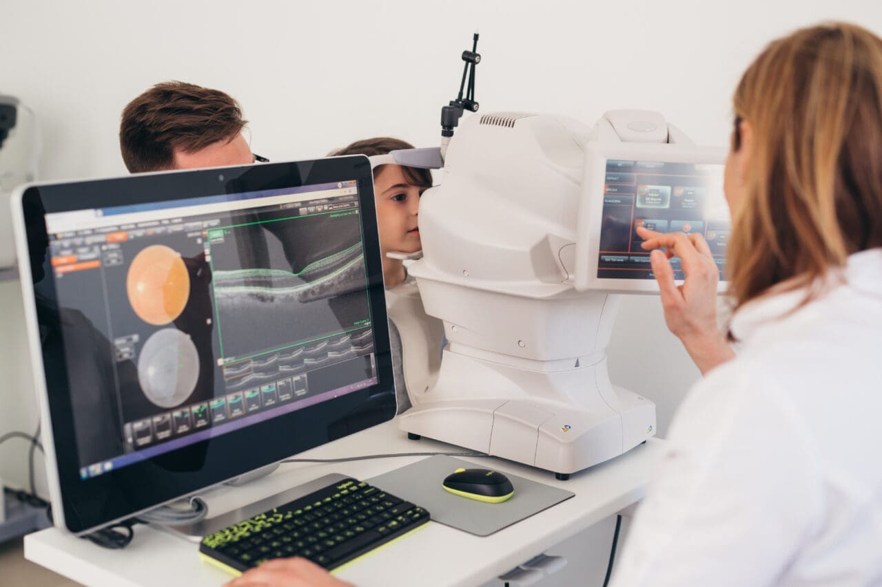 Optician doing eye examination on child, which is displayed on computer screen