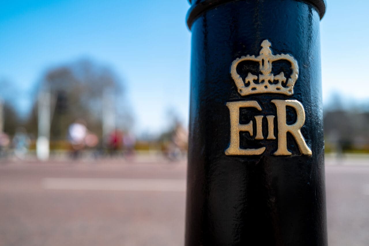 Bollard with Queen Elizabeth 2nd insignia outside of Buckingham Palace, London. Hyde park can be seen behind on a bright sunny day.