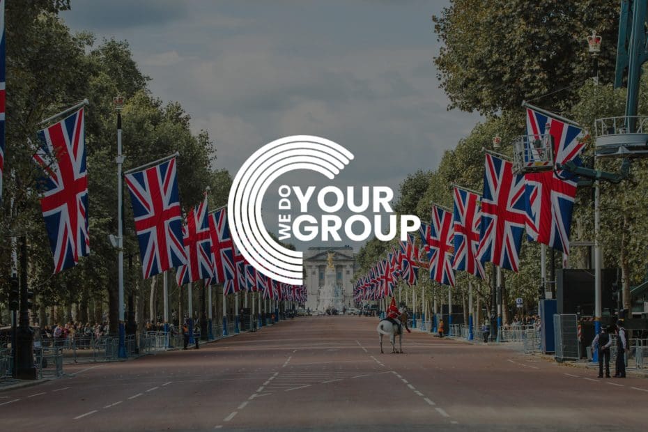 WeDoYourGroup white logo on background of Buckingham palace with United Kingdom flags placed down the road