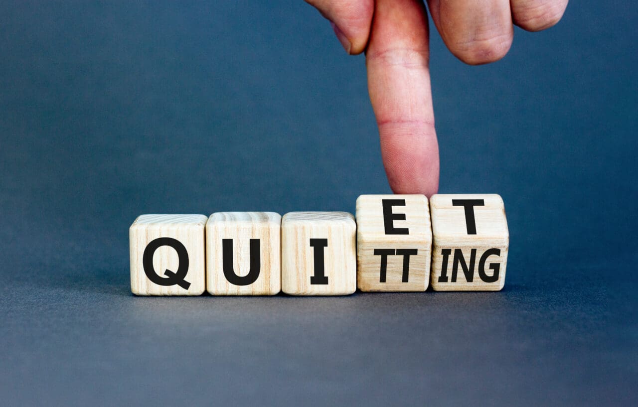 Quiet quitting symbol. Concept words Quiet quitting on wooden cubes. Businessman hand. Beautiful grey table grey background. Business quiet quitting concept. Copy space.