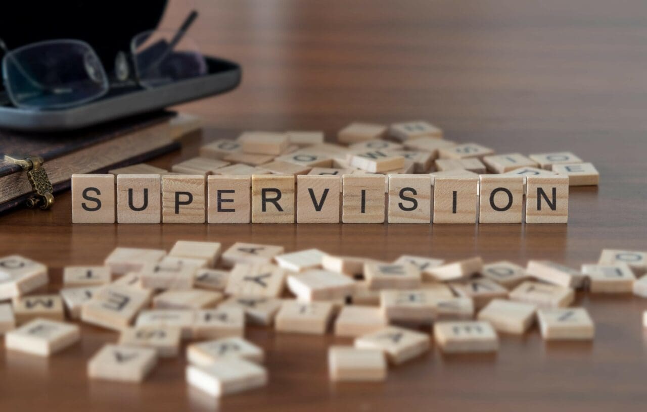 supervision word or concept represented by wooden letter tiles on a wooden table with glasses and a book